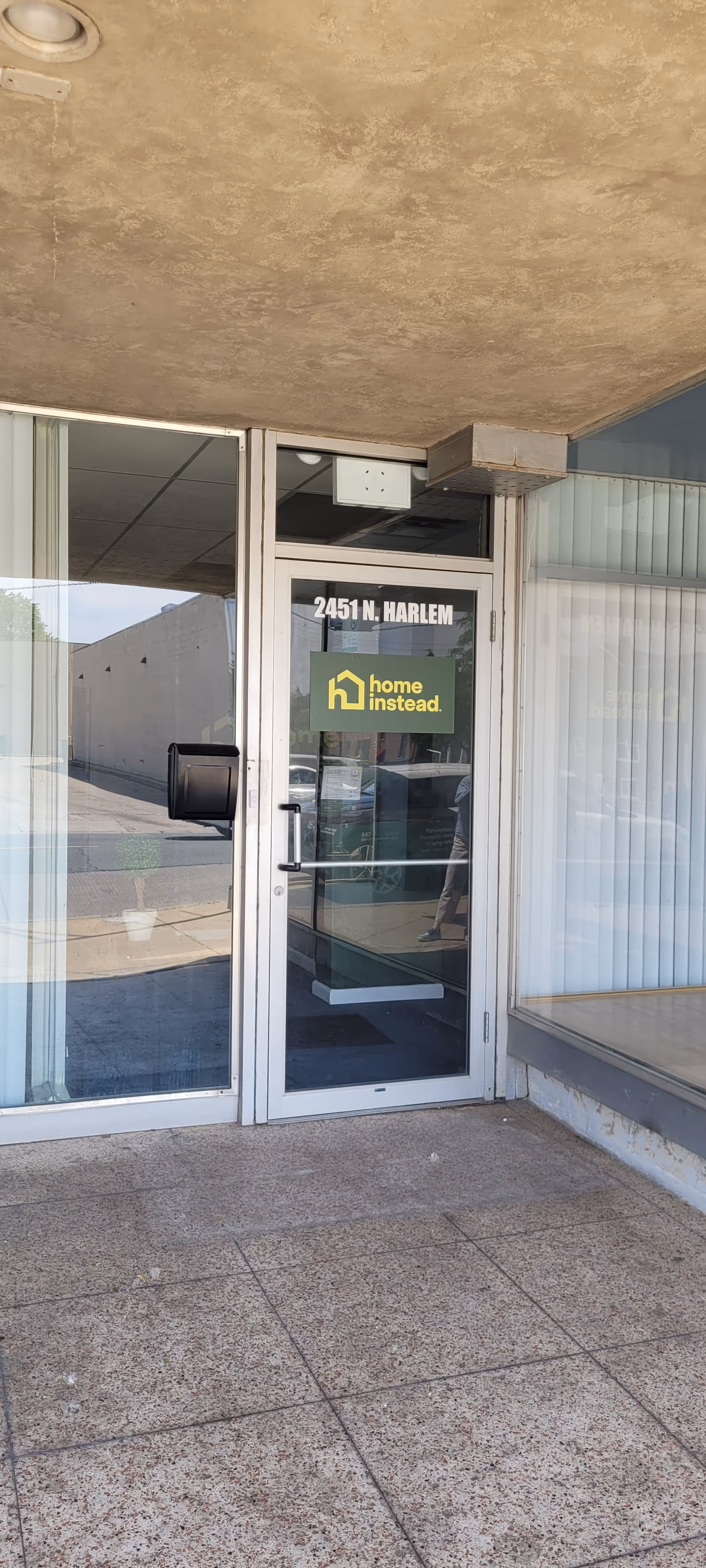 Glass entrance door with Home Instead sign, address 2451 N. Harlem, exterior storefront.