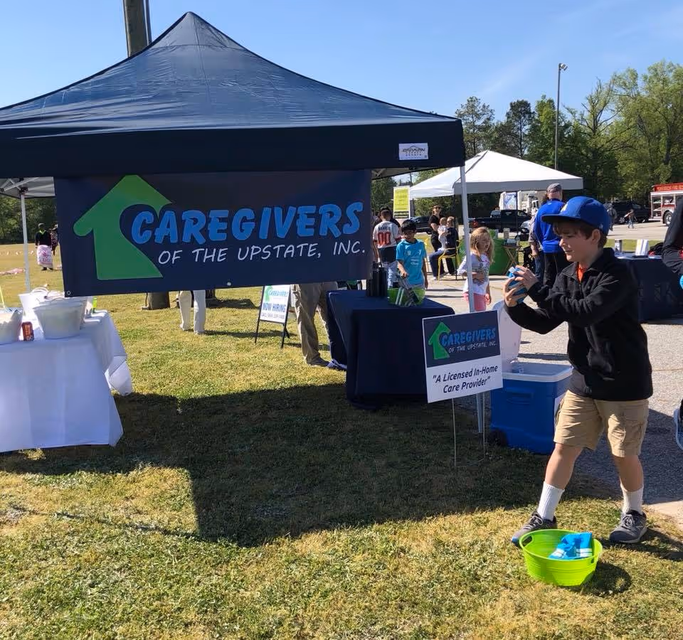 Outdoor event with a Caregivers of the Upstate booth and attendees.