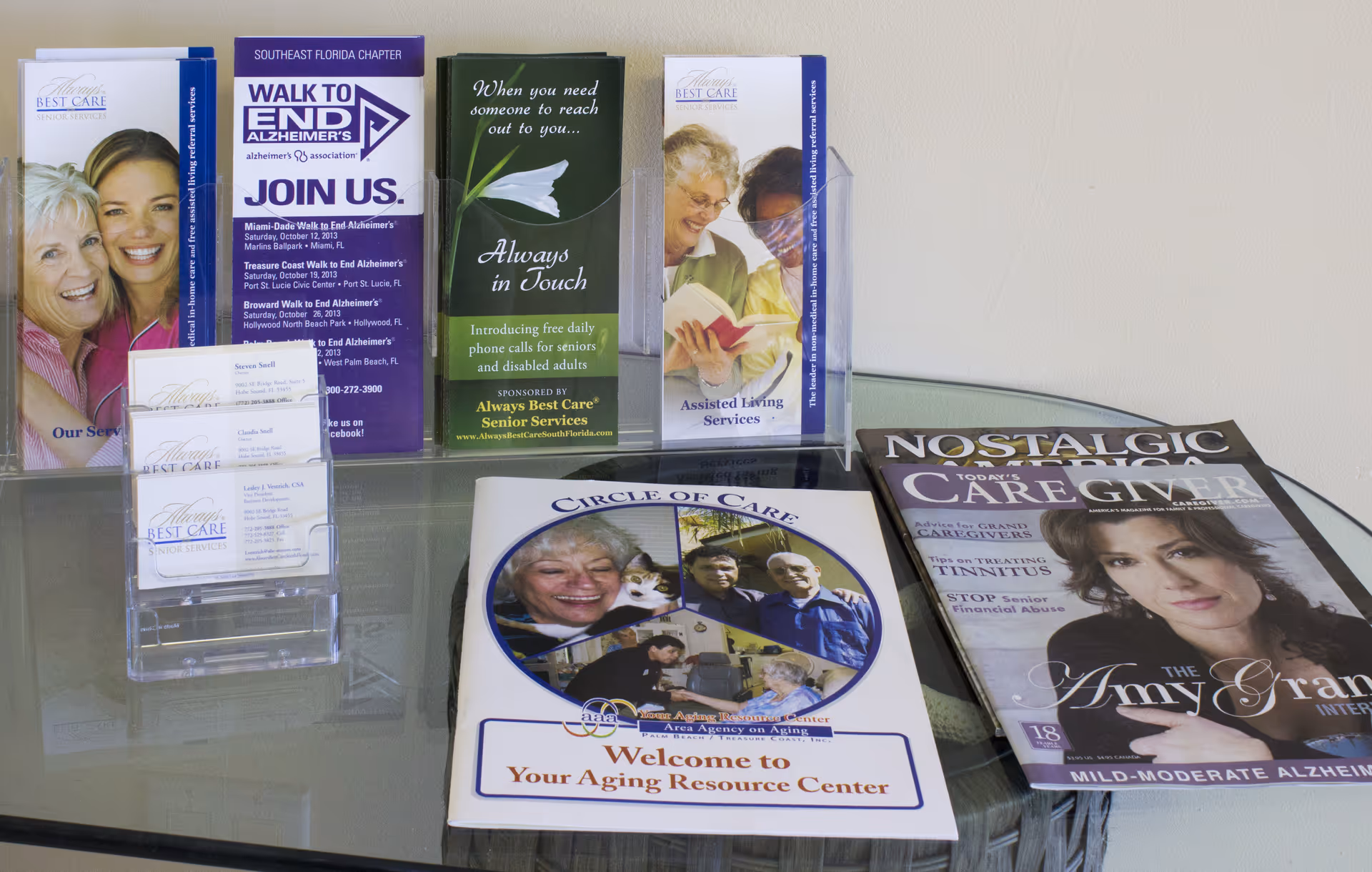 Brochure rack and magazines on glass table in a sunlit interior of a senior care facility.