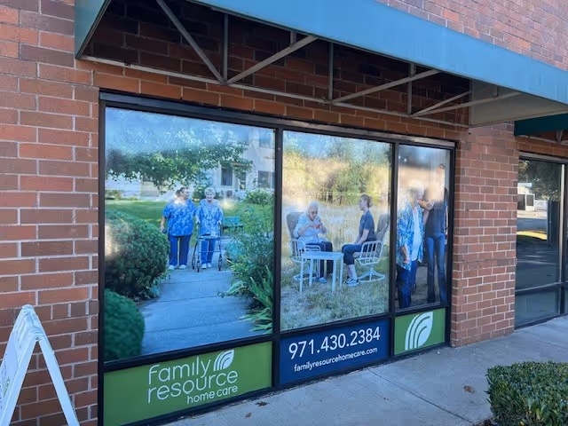 Brick storefront with large display windows featuring seniors and caregivers.