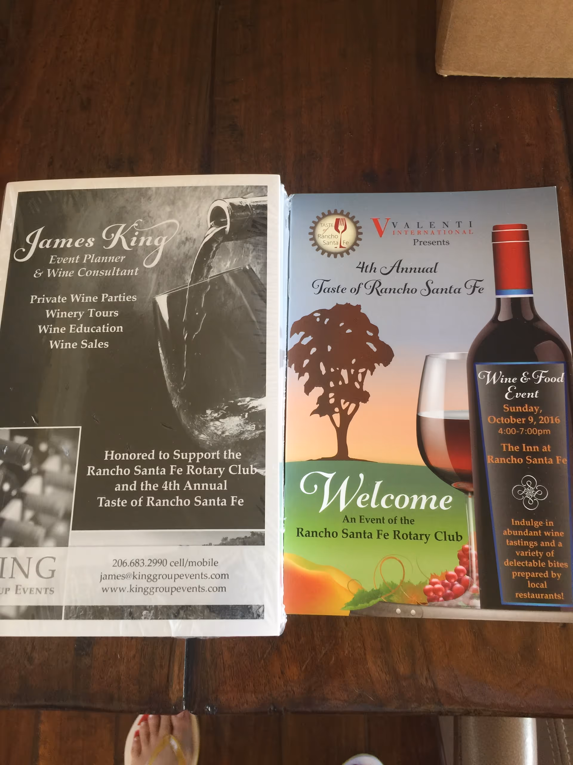Two wine-event brochures rest on a wooden table indoors.