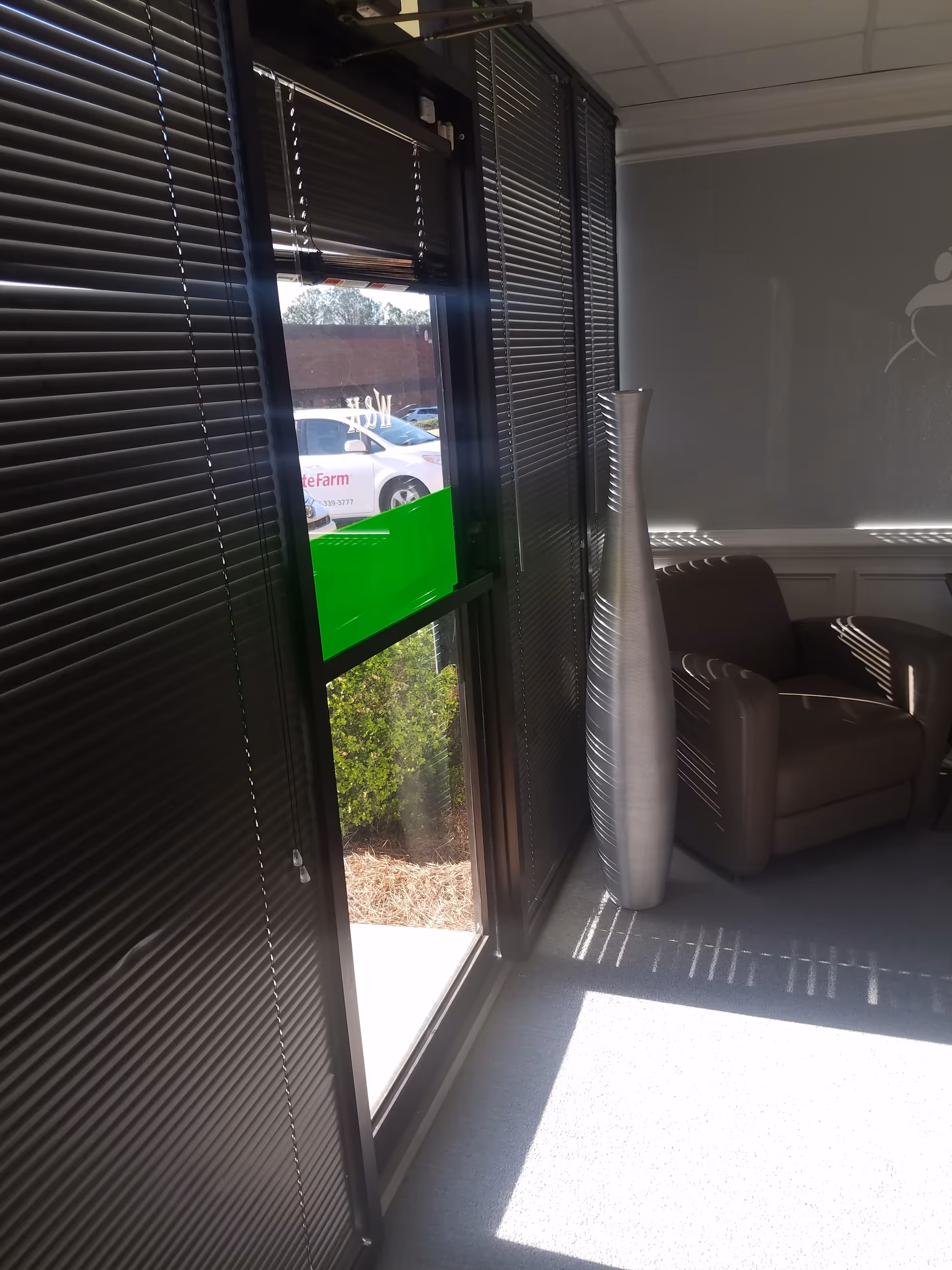 Interior seating area with a large window, vertical blinds, and a tall decorative vase.