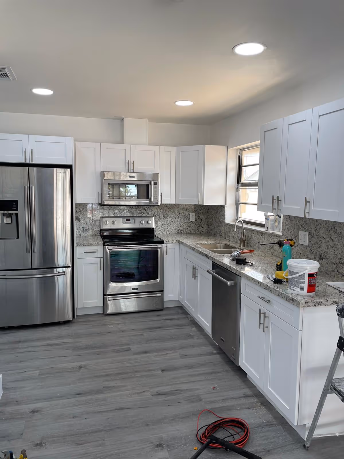 Modern white kitchen with stainless steel appliances, granite countertops, and bright ceiling lights.