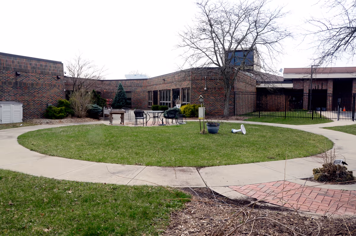 Circular grassy courtyard with patio furniture and a brick building in the background.