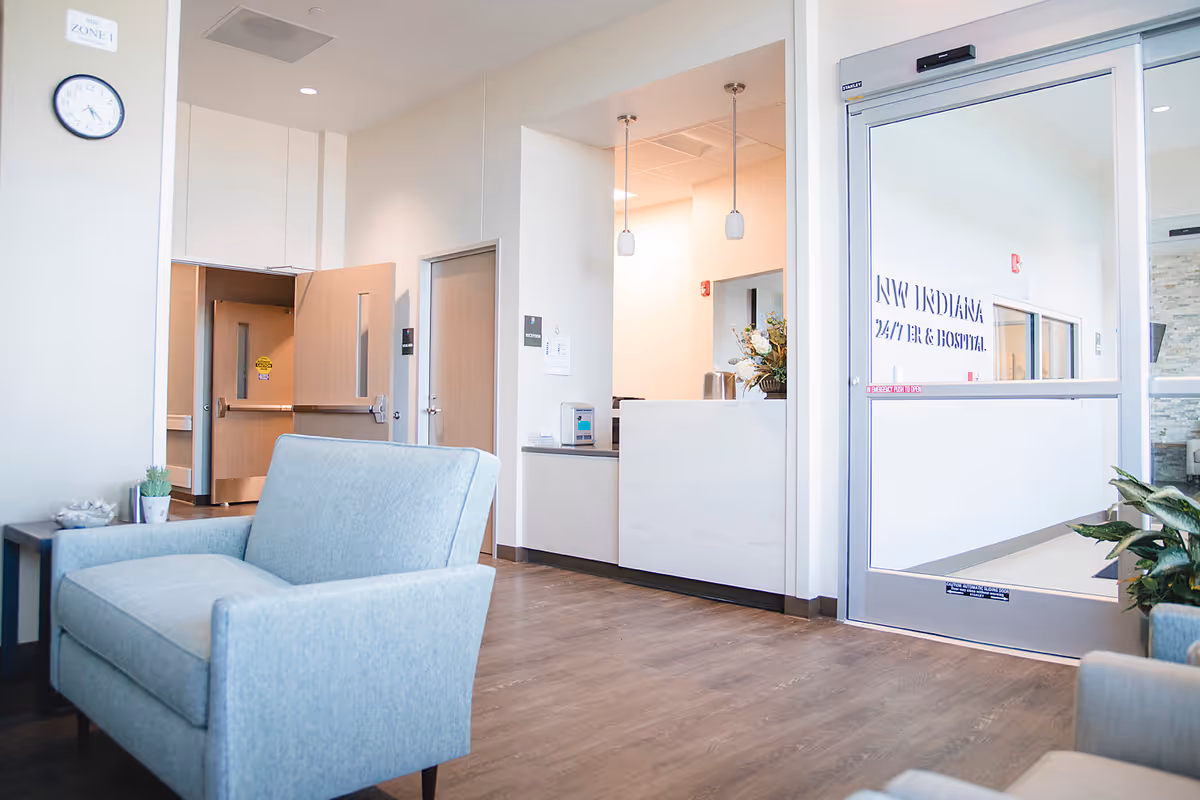 Interior hospital lobby with pale furniture, reception desk, and glass entry door.