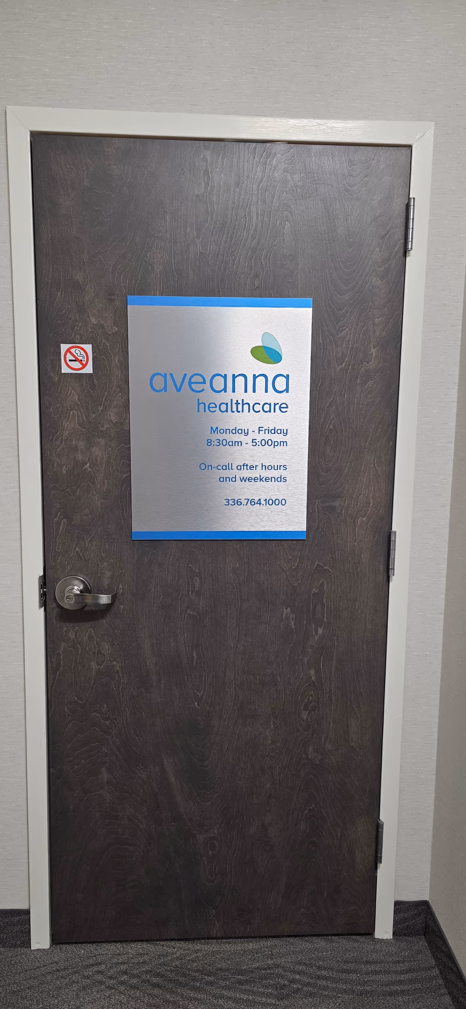 Small Aveanna Healthcare sign on a dark wooden door in a hallway.