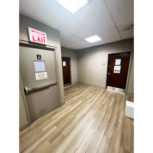 A hallway in a senior living facility with doors, an exit sign, and wood flooring.