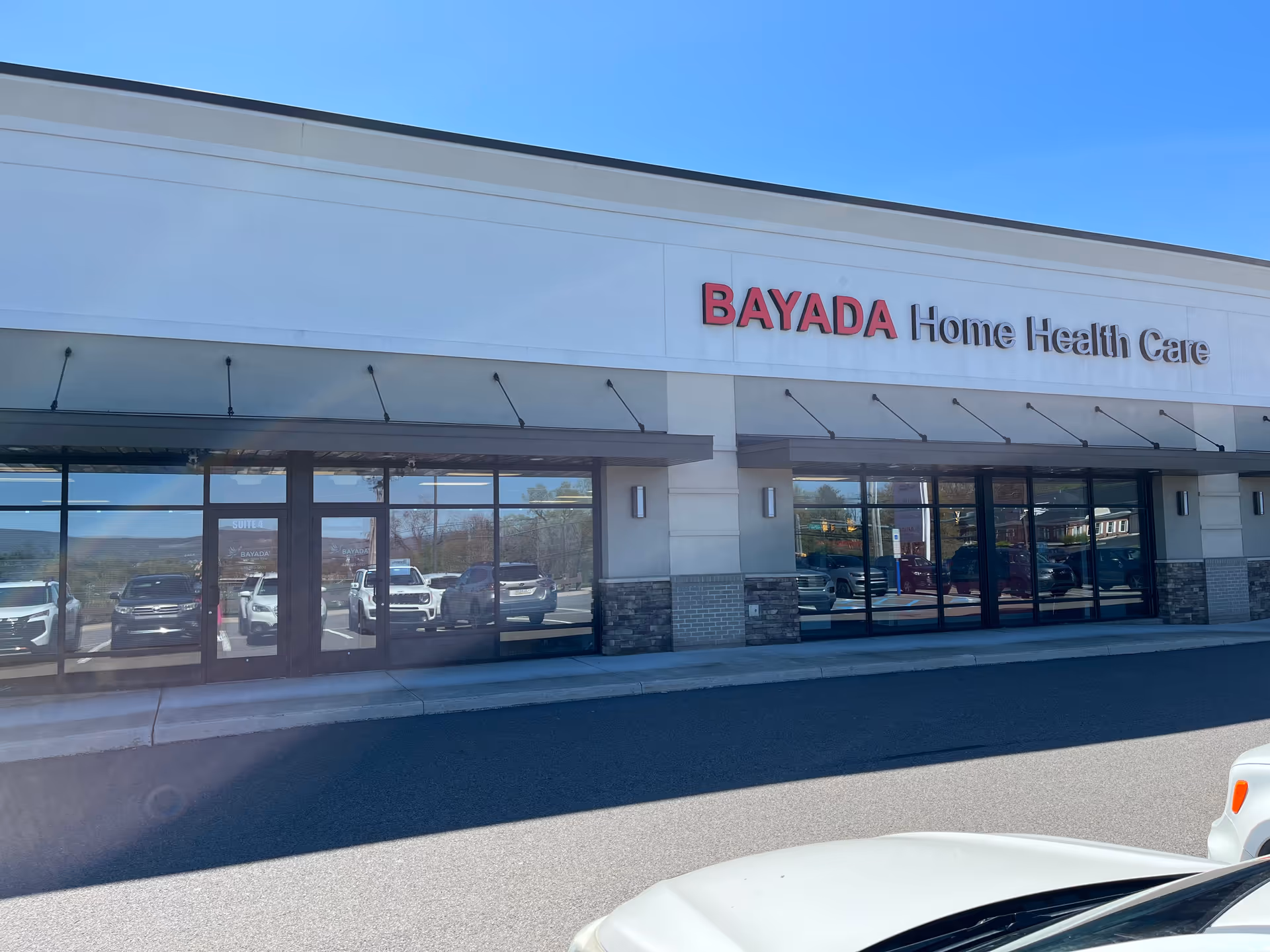 Exterior view of BAYADA Home Health Care storefront with glass doors and parked cars.
