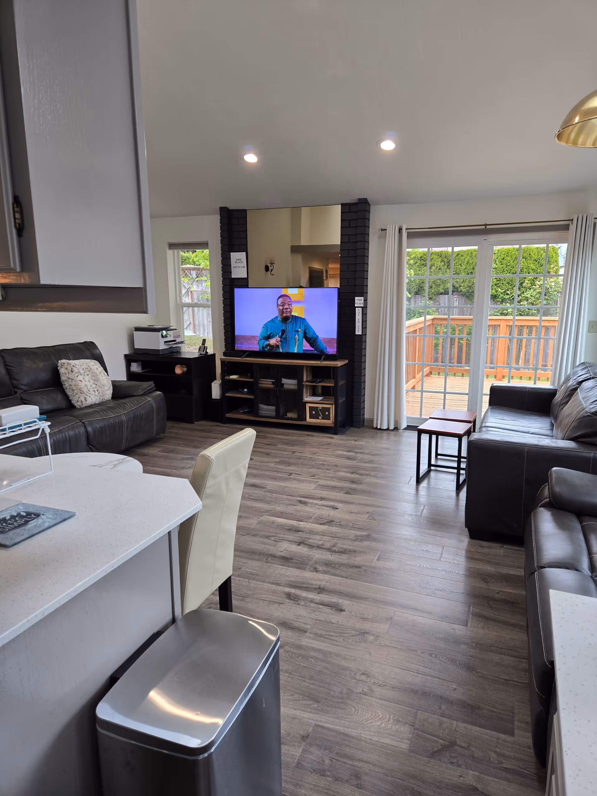Open-concept living room with leather sofas, TV, kitchen island, and sliding deck doors.