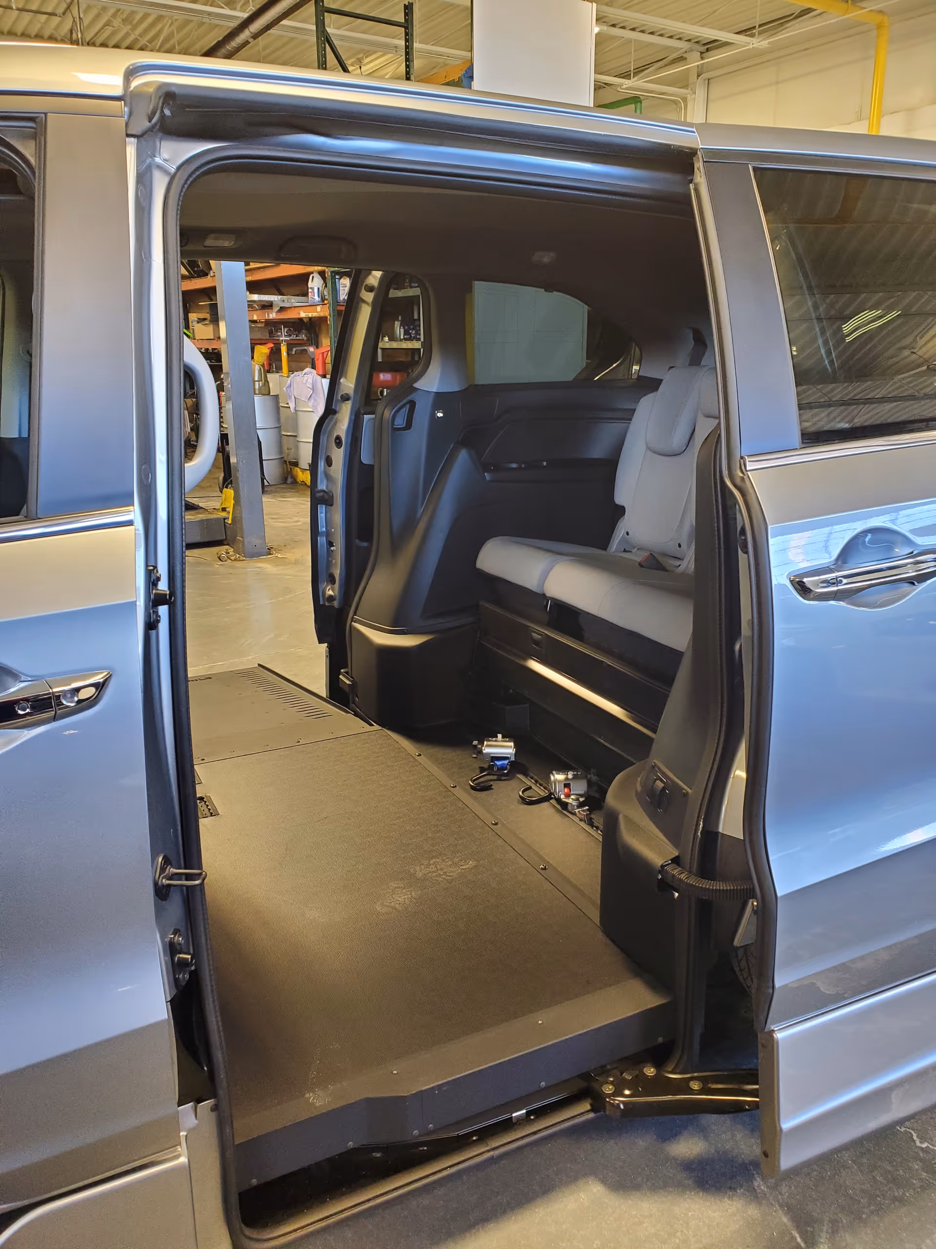 Blue wheelchair-accessible van with lowered floor and ramp inside a workshop.