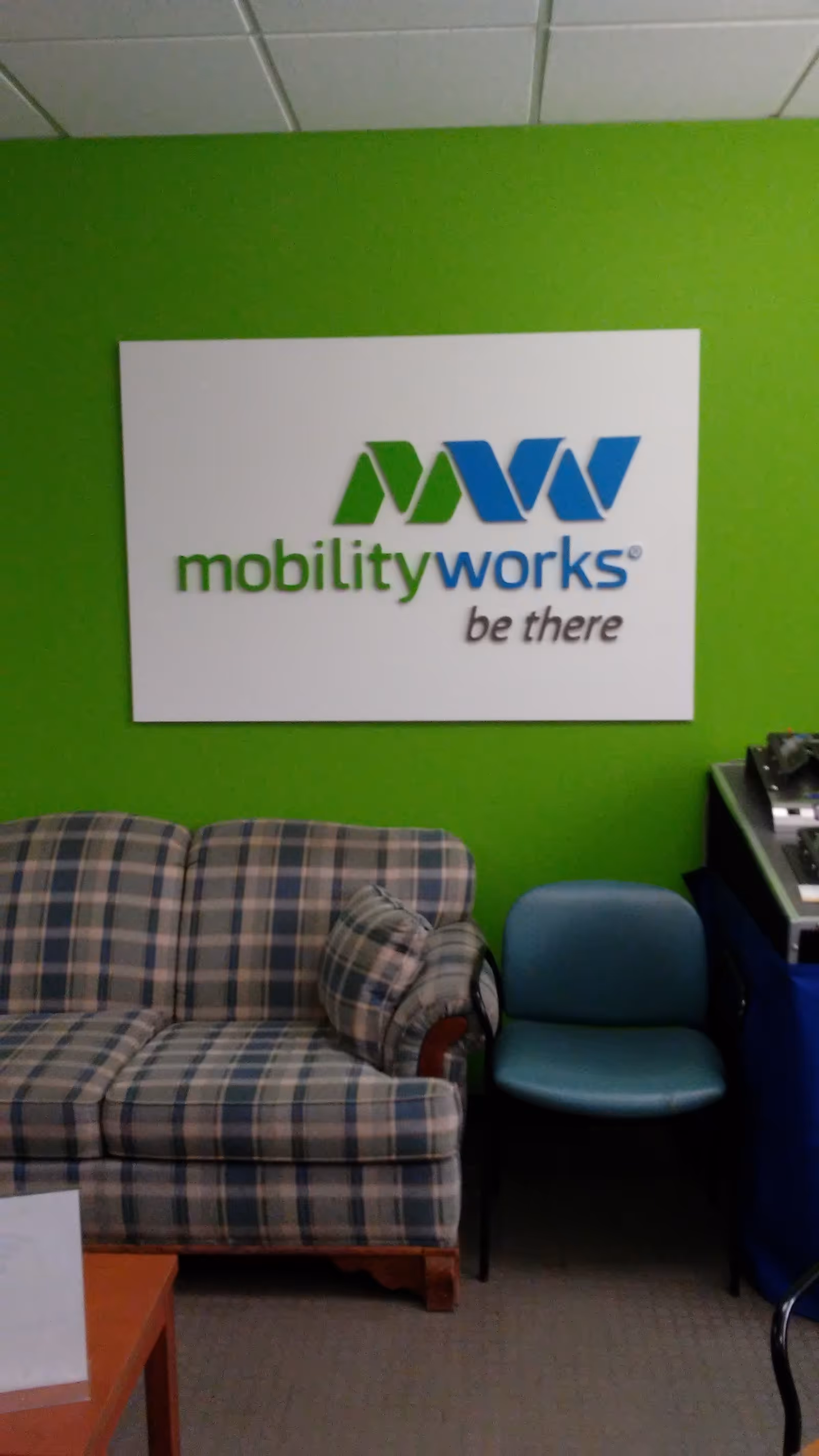 Bright green-walled lobby featuring a MobilityWorks sign and plaid sofa.