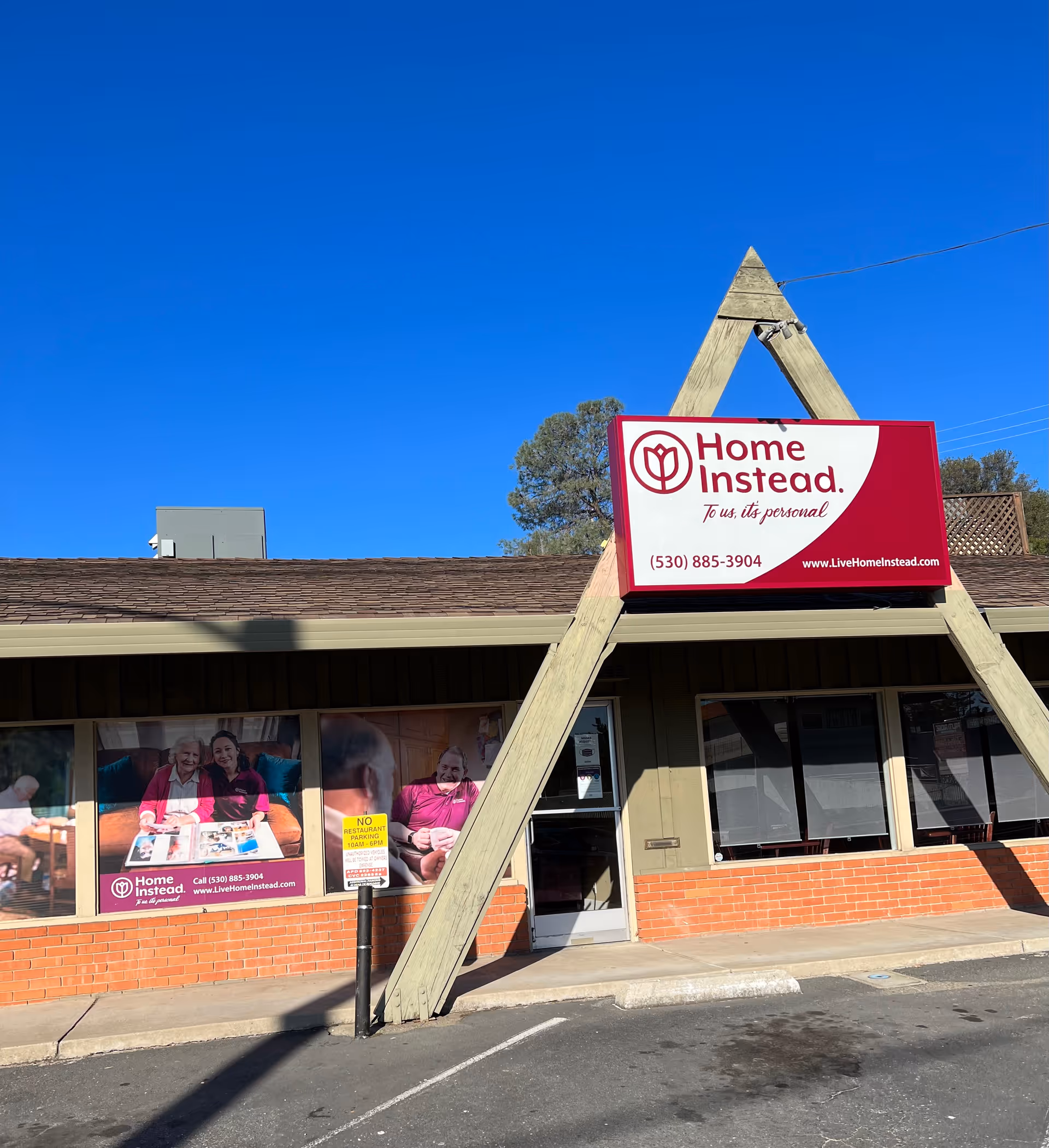 Exterior of a Home Instead center with a large red sign against a bright blue sky.