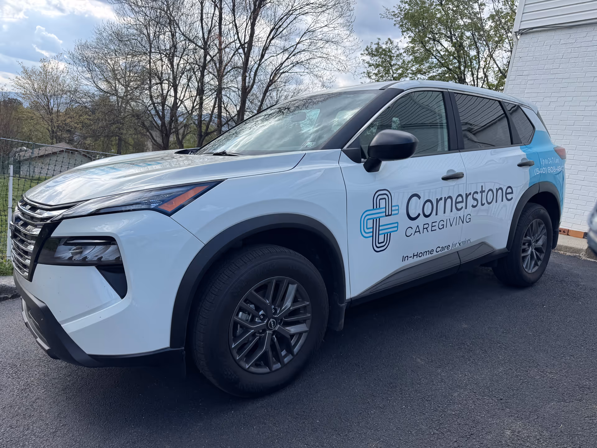 A white Cornerstone Caregiving vehicle parked outside a building with trees in background.