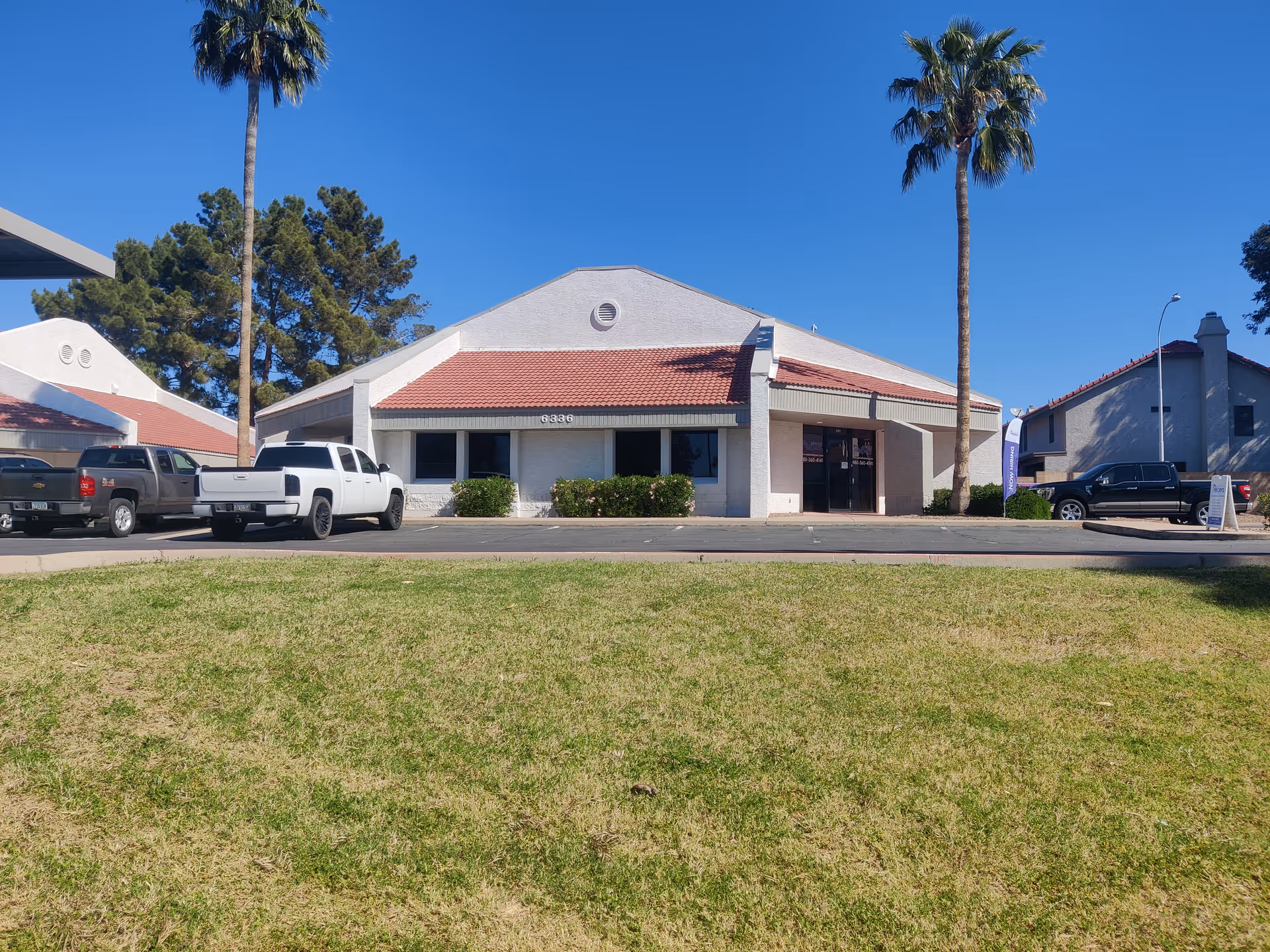 Front view of a Senior Helpers facility with cars and palm trees.