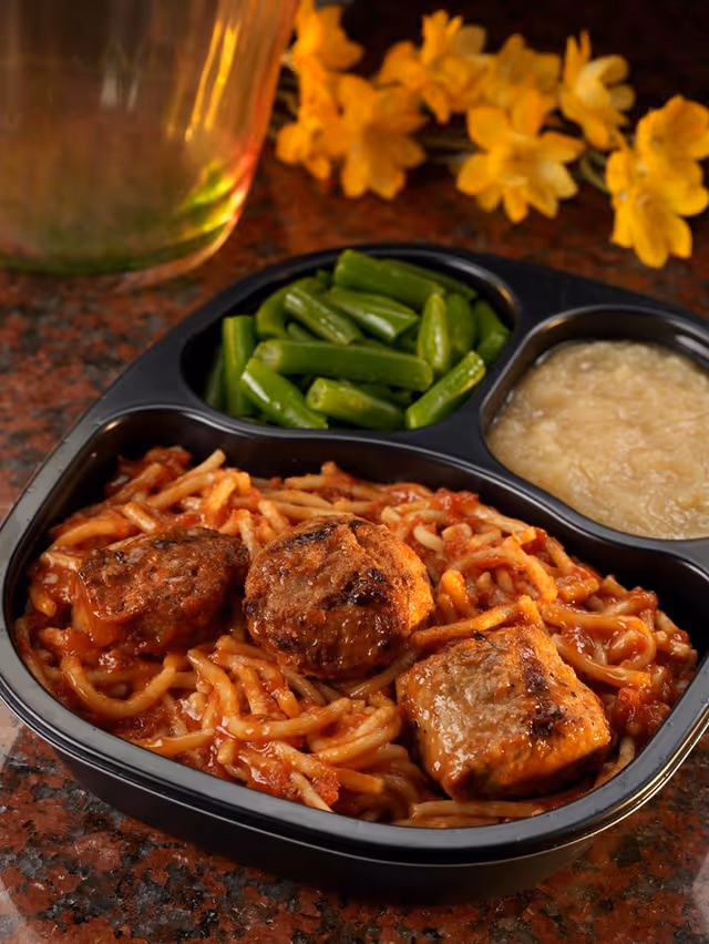 Meal tray with meatballs and pasta, green beans, and applesauce on a divided tray.