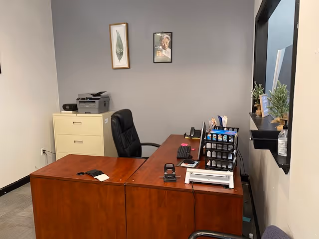 A furnished interior office with a wooden desk, chair, printer, and filing cabinet.
