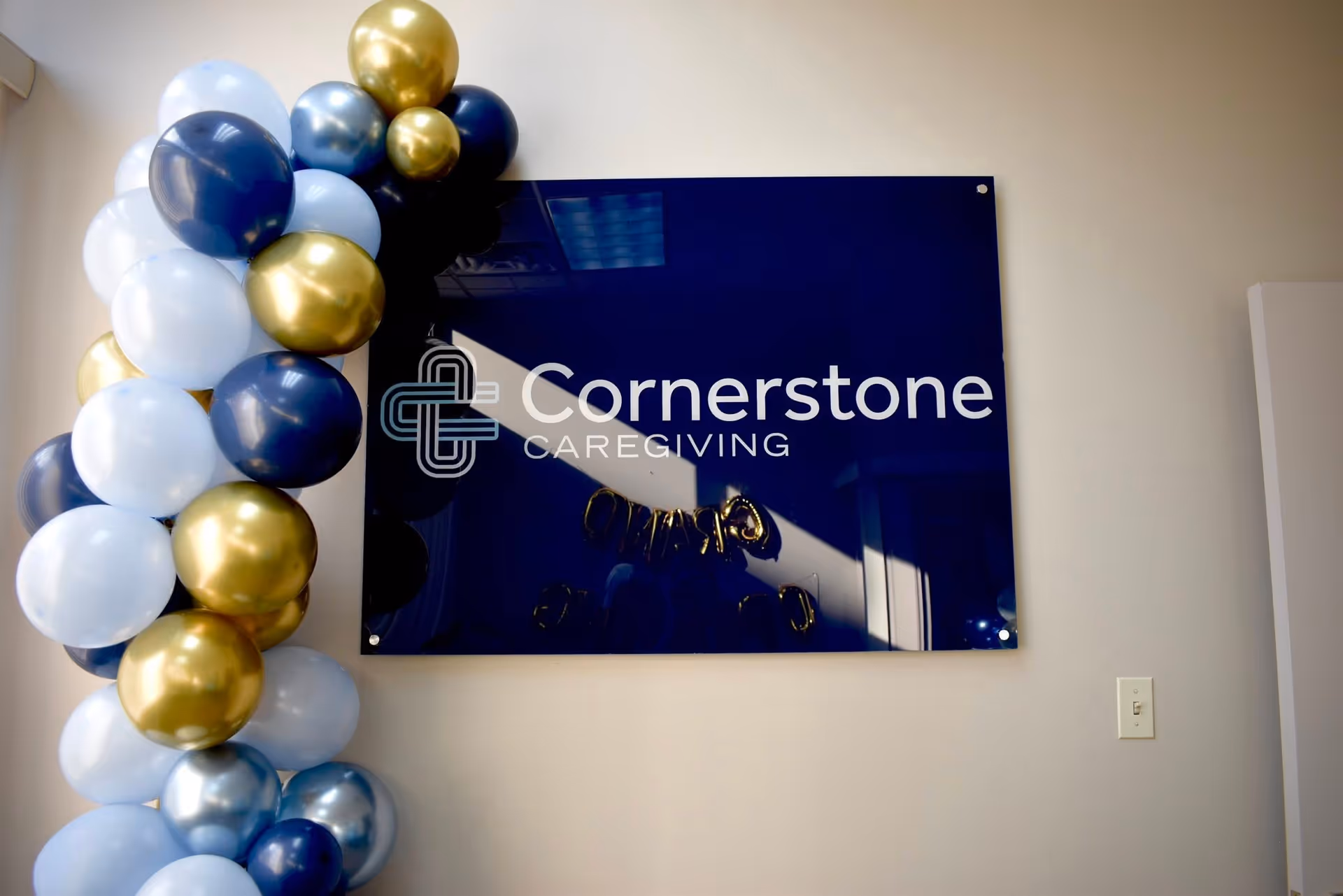 Indoor wall featuring a Cornerstone Caregiving sign with blue and gold balloons.