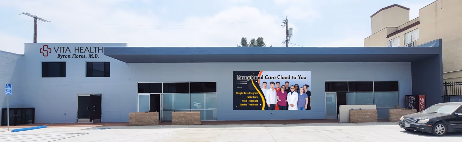 Blue medical facility storefront with Vita Health sign, banner, and parked car outside.
