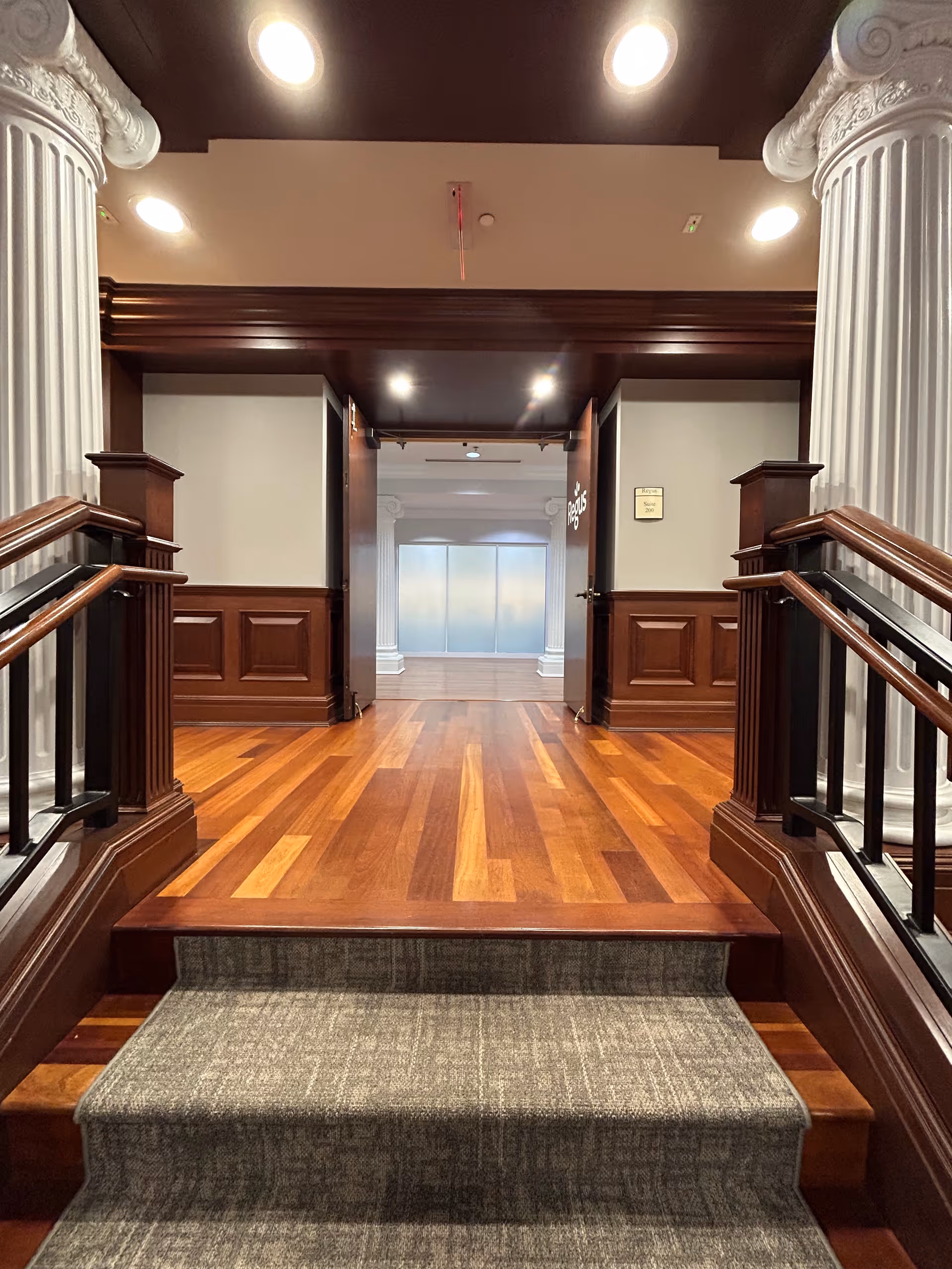 Elegant interior hallway with wooden floors, stairs, columns, and double doors at far end.