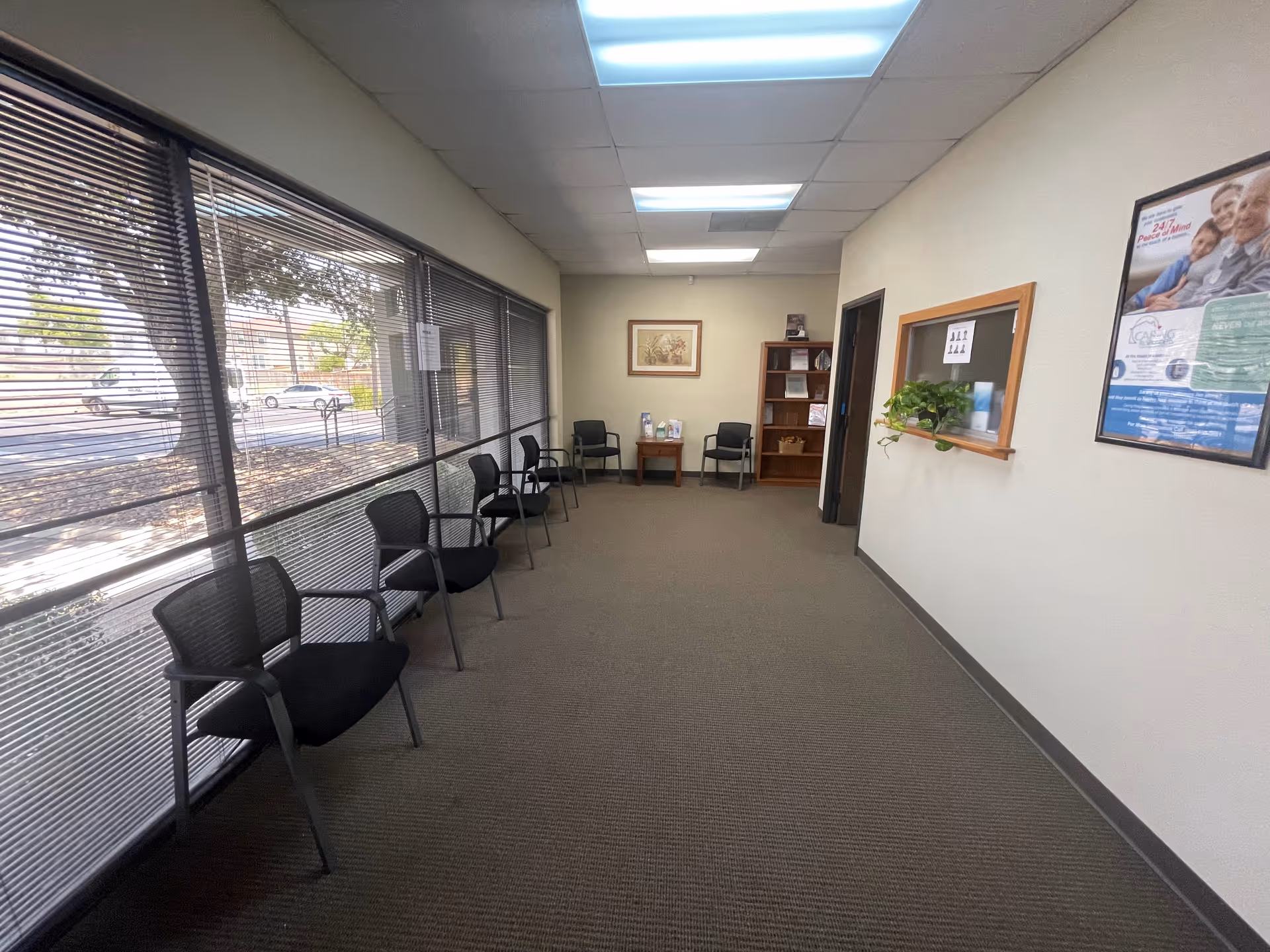 A long interior corridor with windows and a row of chairs in a waiting area.