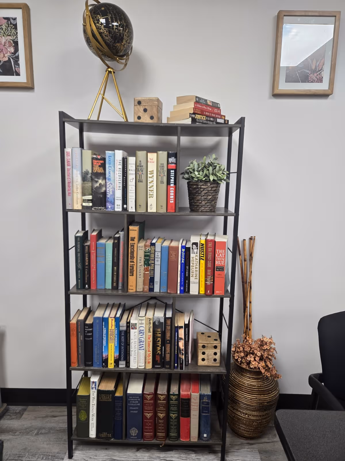 Metal bookshelf loaded with books, globe decor, plant, and framed art.