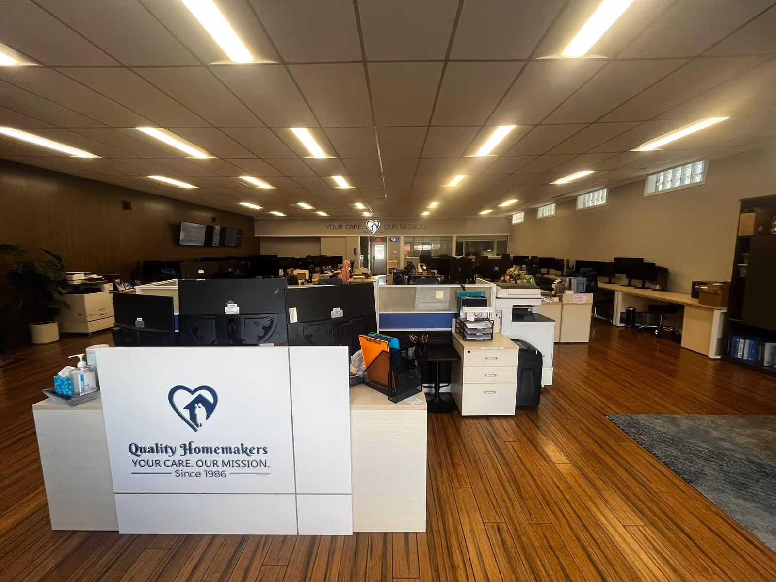 Reception area inside Quality Homemakers facility with cubicles, computers, and office furniture.