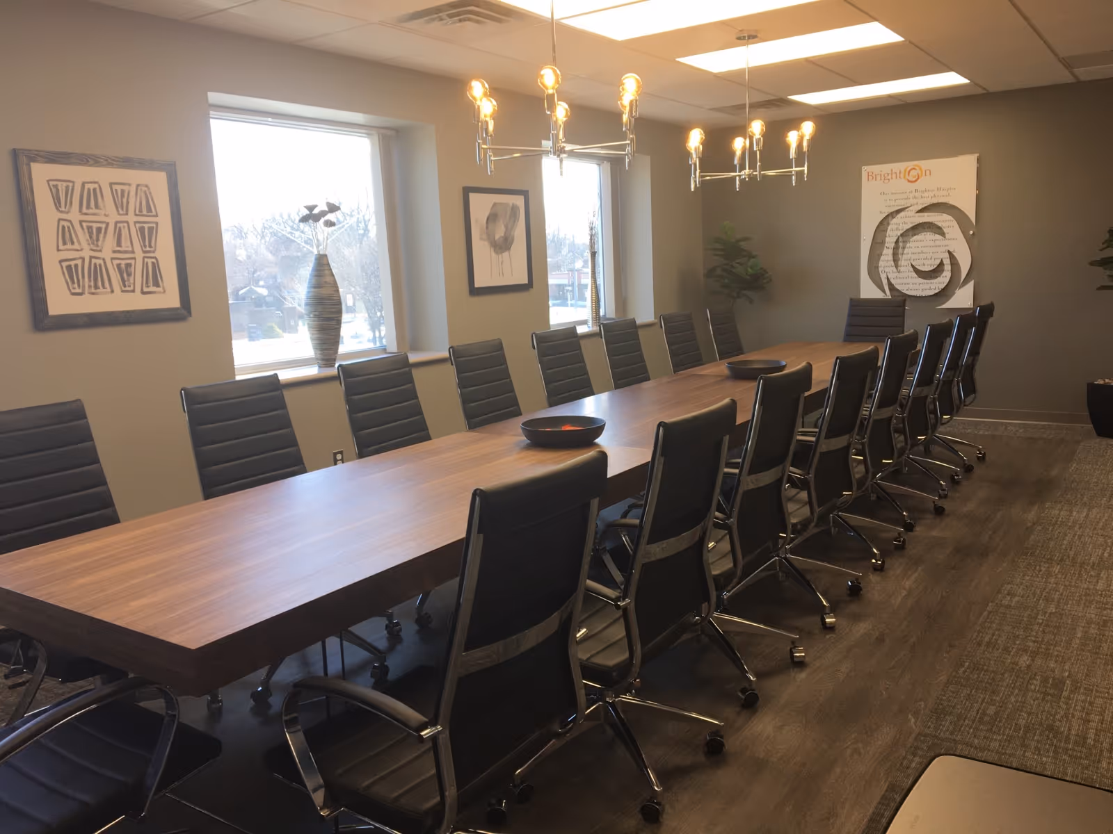 Long wooden conference table with black chairs in a bright meeting room.
