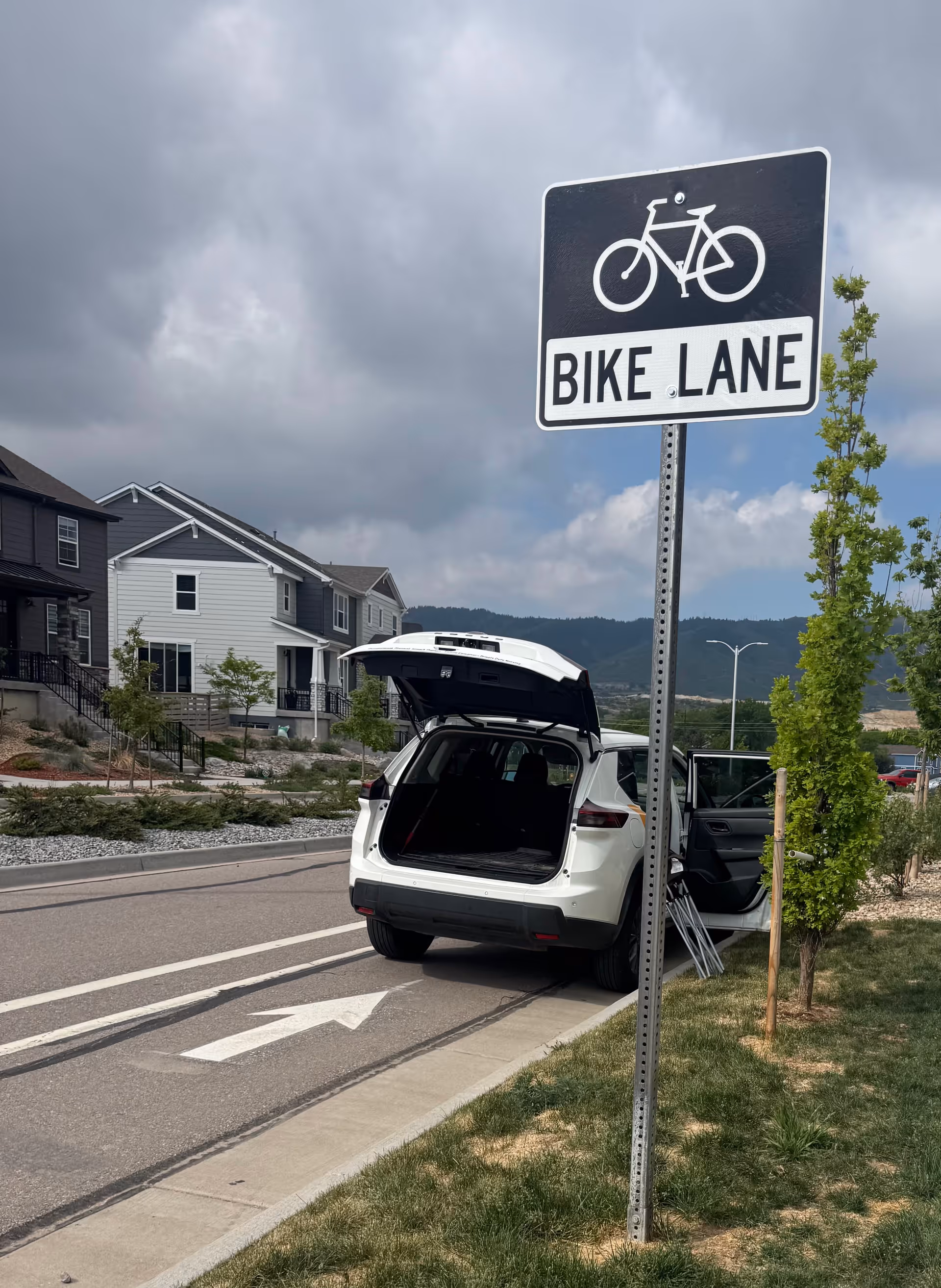 White SUV with open trunk parked on a suburban street next to a bike-lane sign.