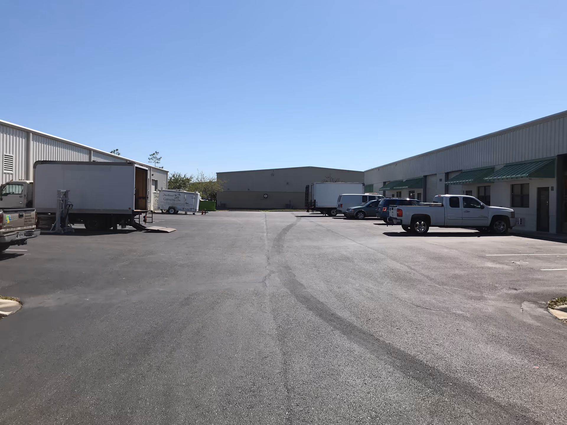 Outdoor parking lot with delivery trucks beside warehouse buildings and loading docks.