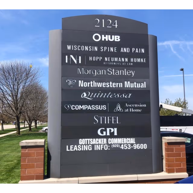 Tall outdoor sign with multiple business names including Ascension at Home and Compassus on a plaza.