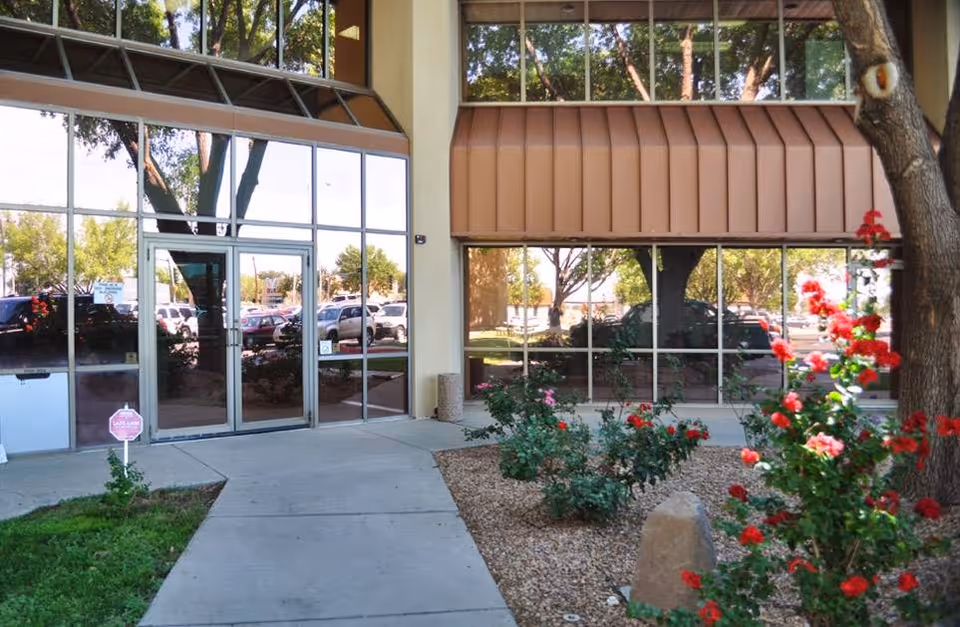 Entrance to Ambercare facility with glass doors, large windows, and landscaped shrubs.