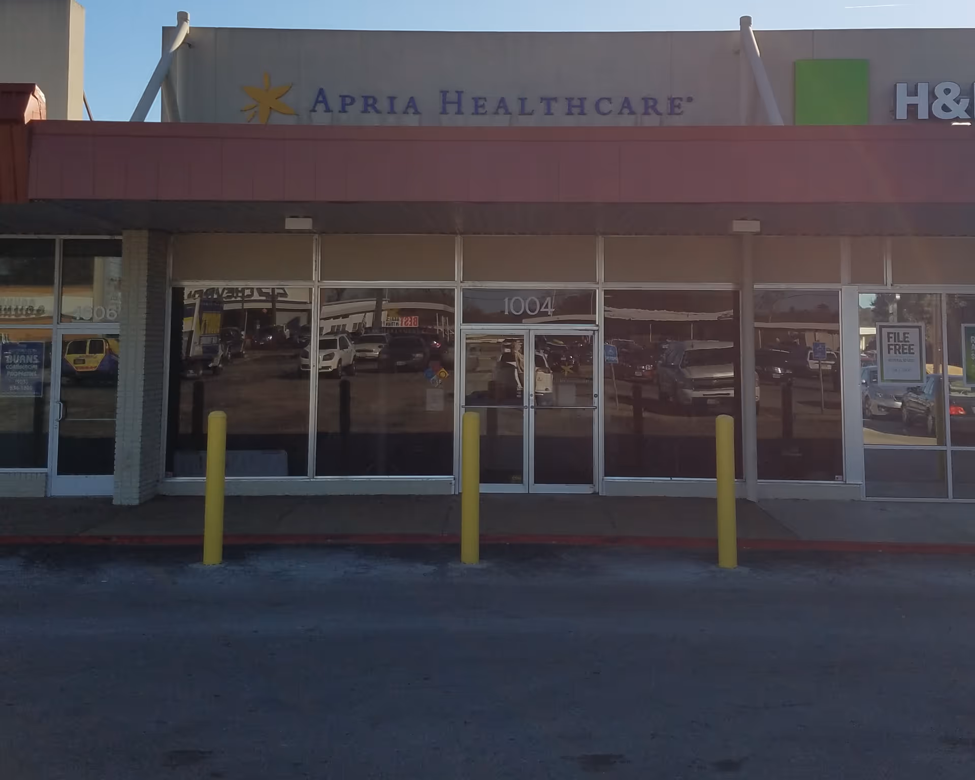 Storefront displaying an Apria Healthcare sign with glass doors and a parking lot.