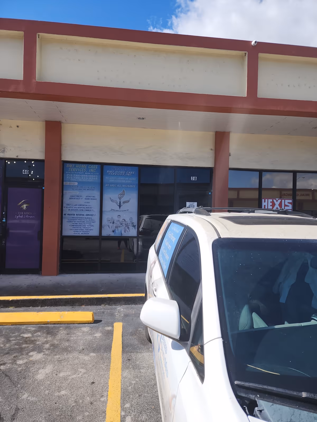 Exterior view of a storefront with signage and a parked white SUV in front.