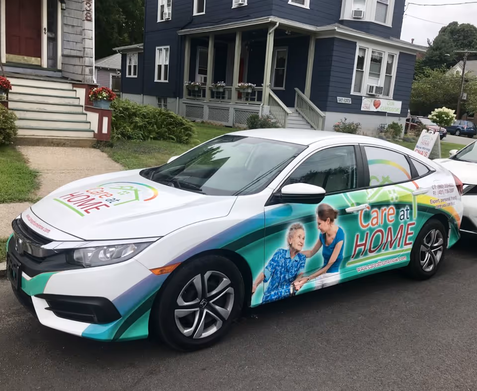 Branding car for Care At Home parked on a residential street beside a blue house.