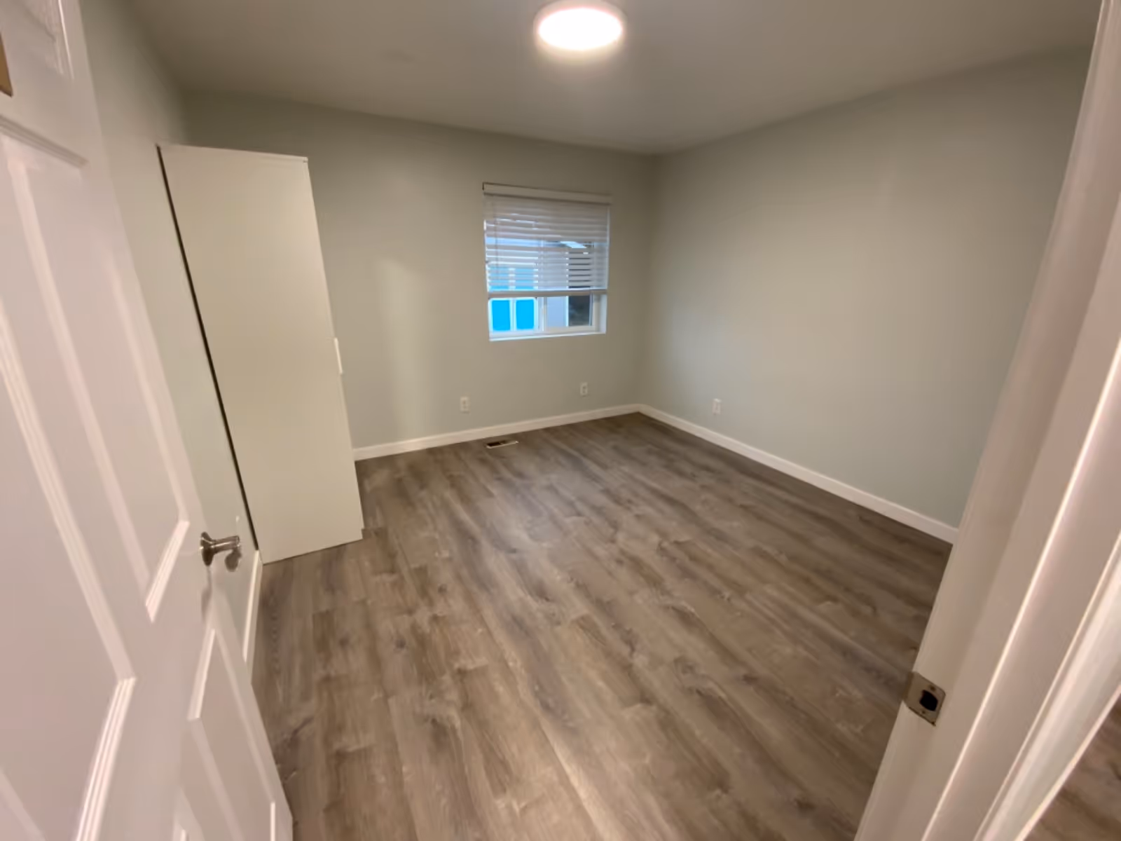 Empty neutral-toned bedroom with a white closet, window, and wood flooring.
