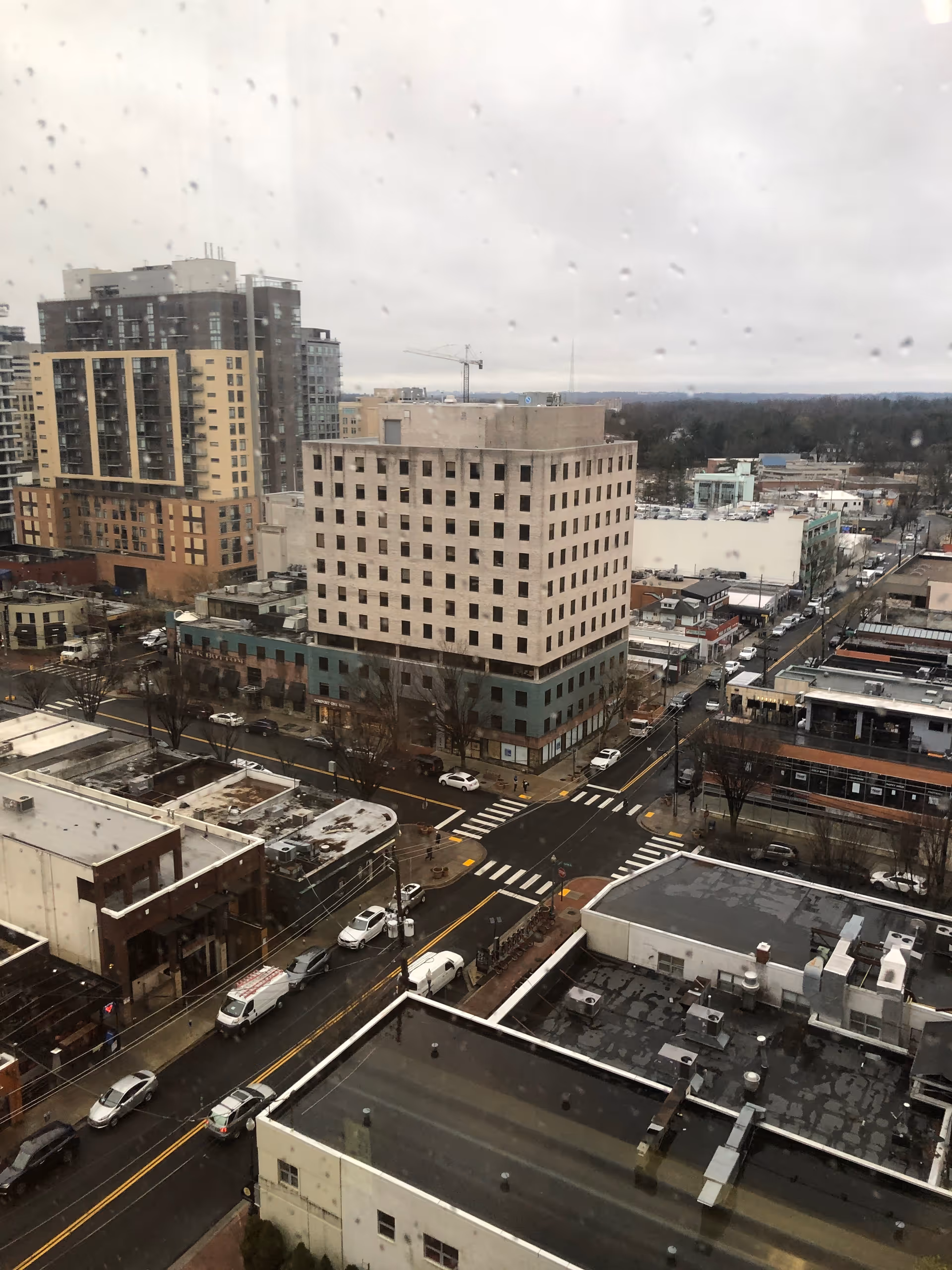 Rainy cityscape with tall buildings and grid-like streets seen from a high window.