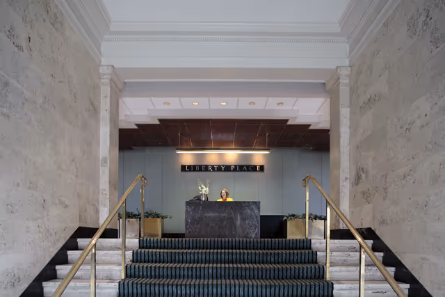 Interior lobby with marble walls, carpeted stairs, and a receptionist at a dark front desk.