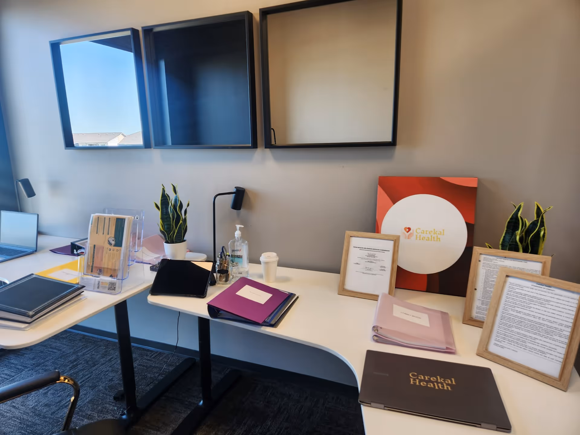 Modern office desk with documents, plants, and Carekal Health branding against a gray wall.