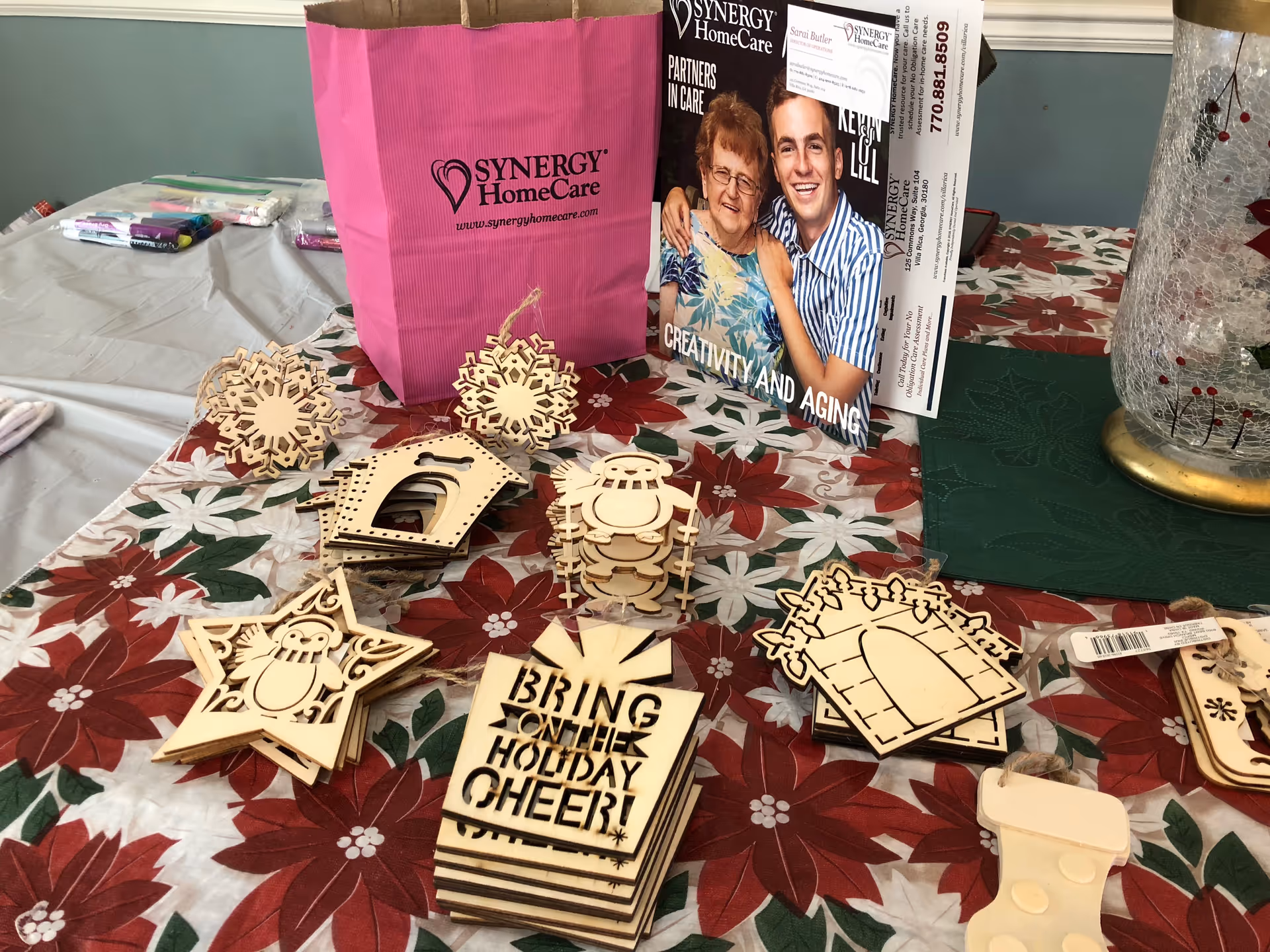 Indoor craft table with wooden shapes and a pink SYNERGY HomeCare bag.