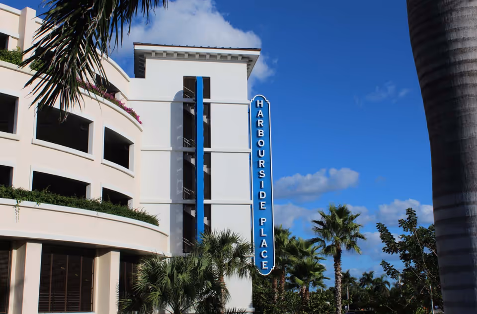 Exterior view of a white multi-story building with a blue Harbourside Place sign and palm trees.