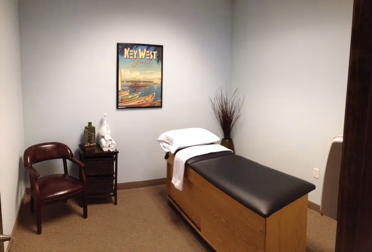 A therapy room with a treatment table, chair, towels, and wall art.