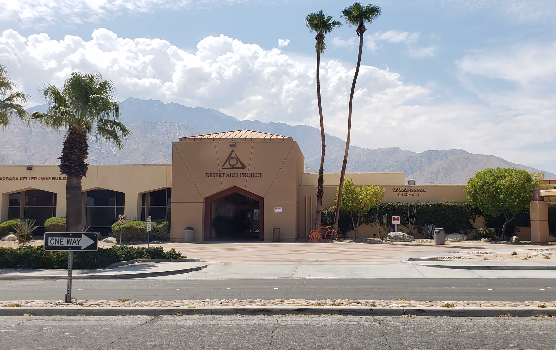 Exterior view of a tan medical building with Desert AIDS Project signage and palm trees.