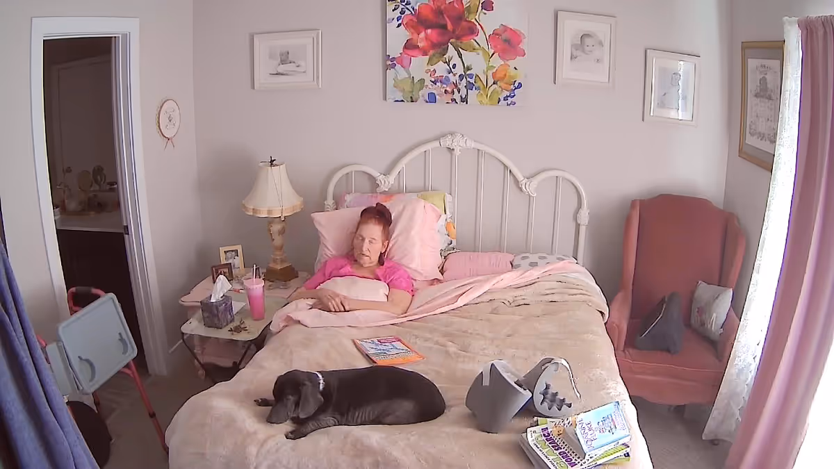 Resident resting in a pink-themed bedroom with a dog on the bed.