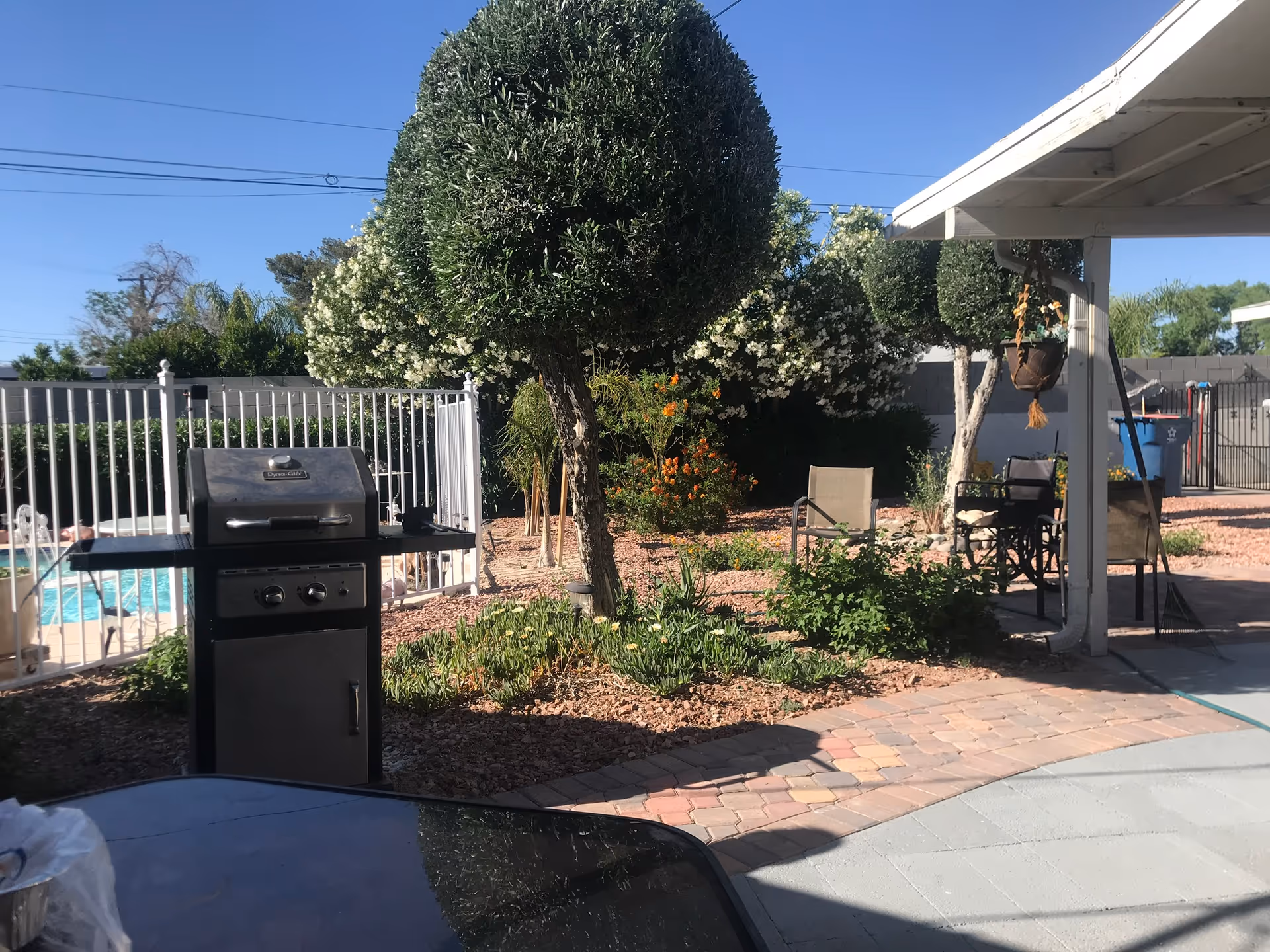 Outdoor patio area with a grill, seating, and a fenced pool.