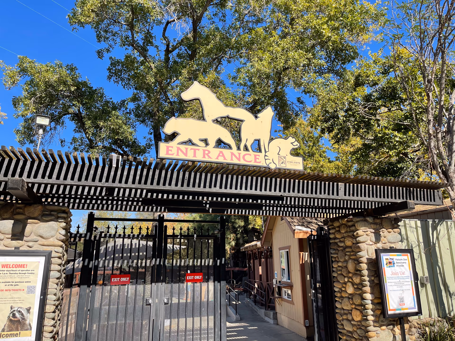 Gated building entrance with stone pillars and decorative horse silhouettes against a blue sky.