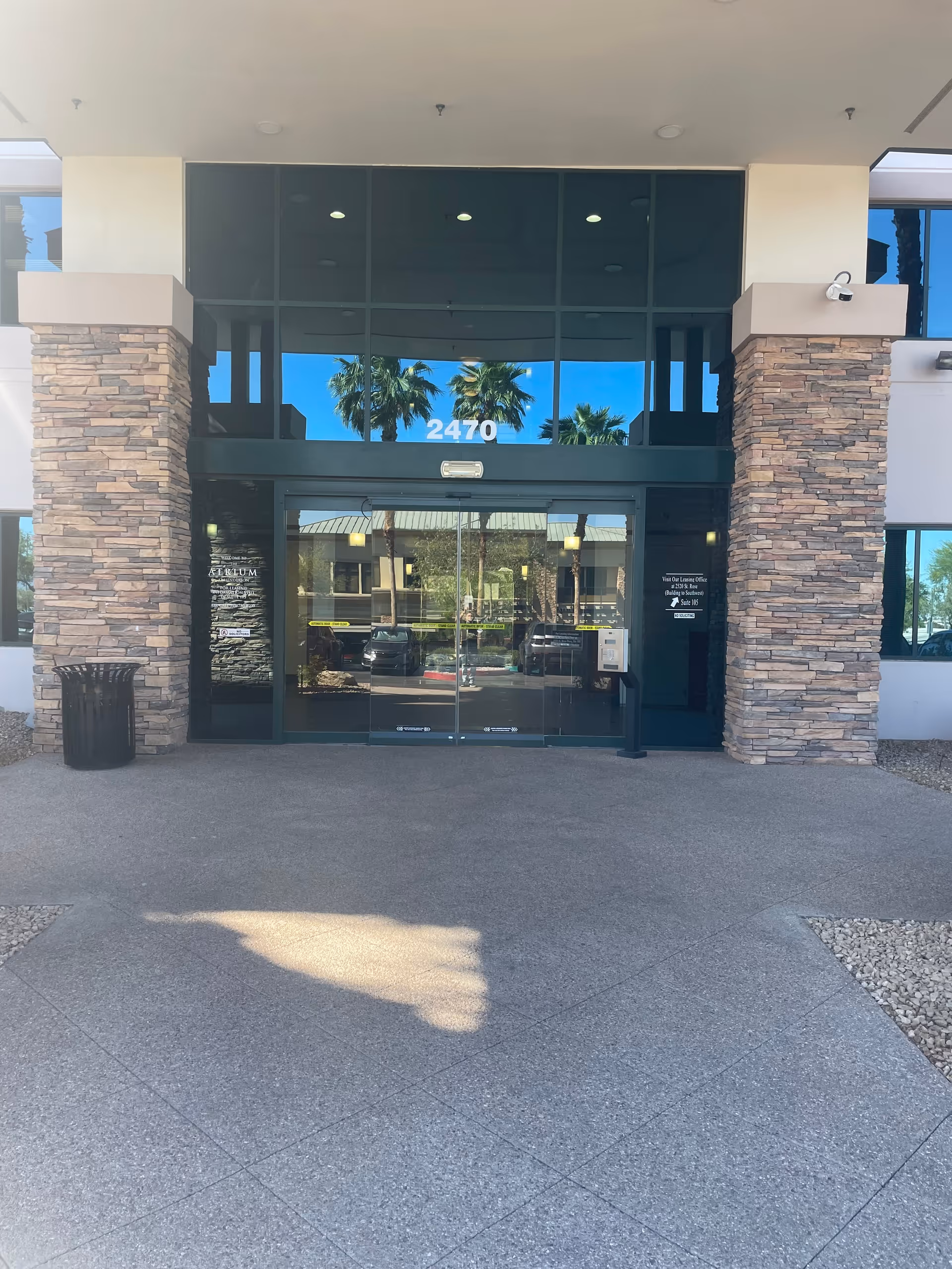 Glass entrance with stone pillars, 2470, and palm reflections at Touching Hearts At Home.
