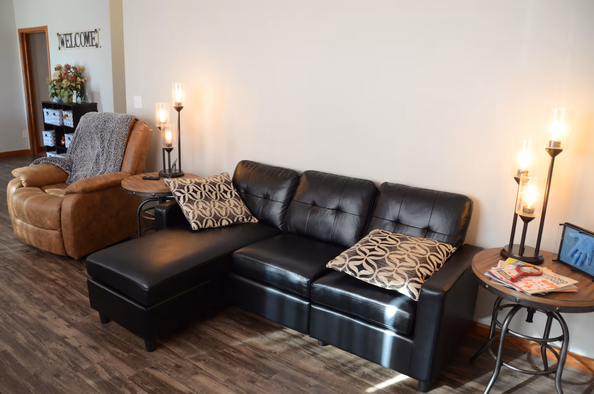 Common living area with black leather sofa, brown recliner, cushions, and side tables.