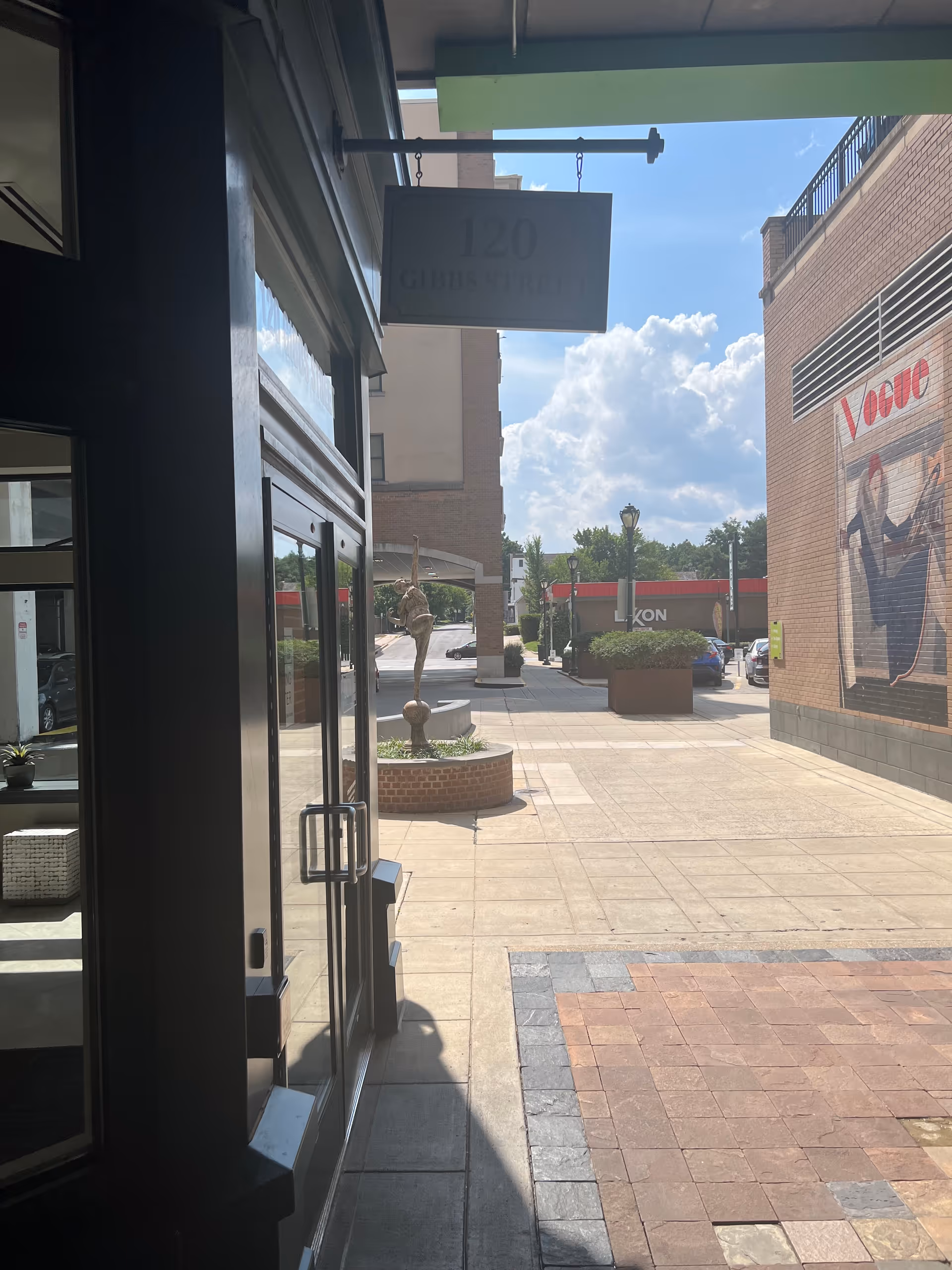 From inside a doorway, a sunny sidewalk with planters and a mural is visible.