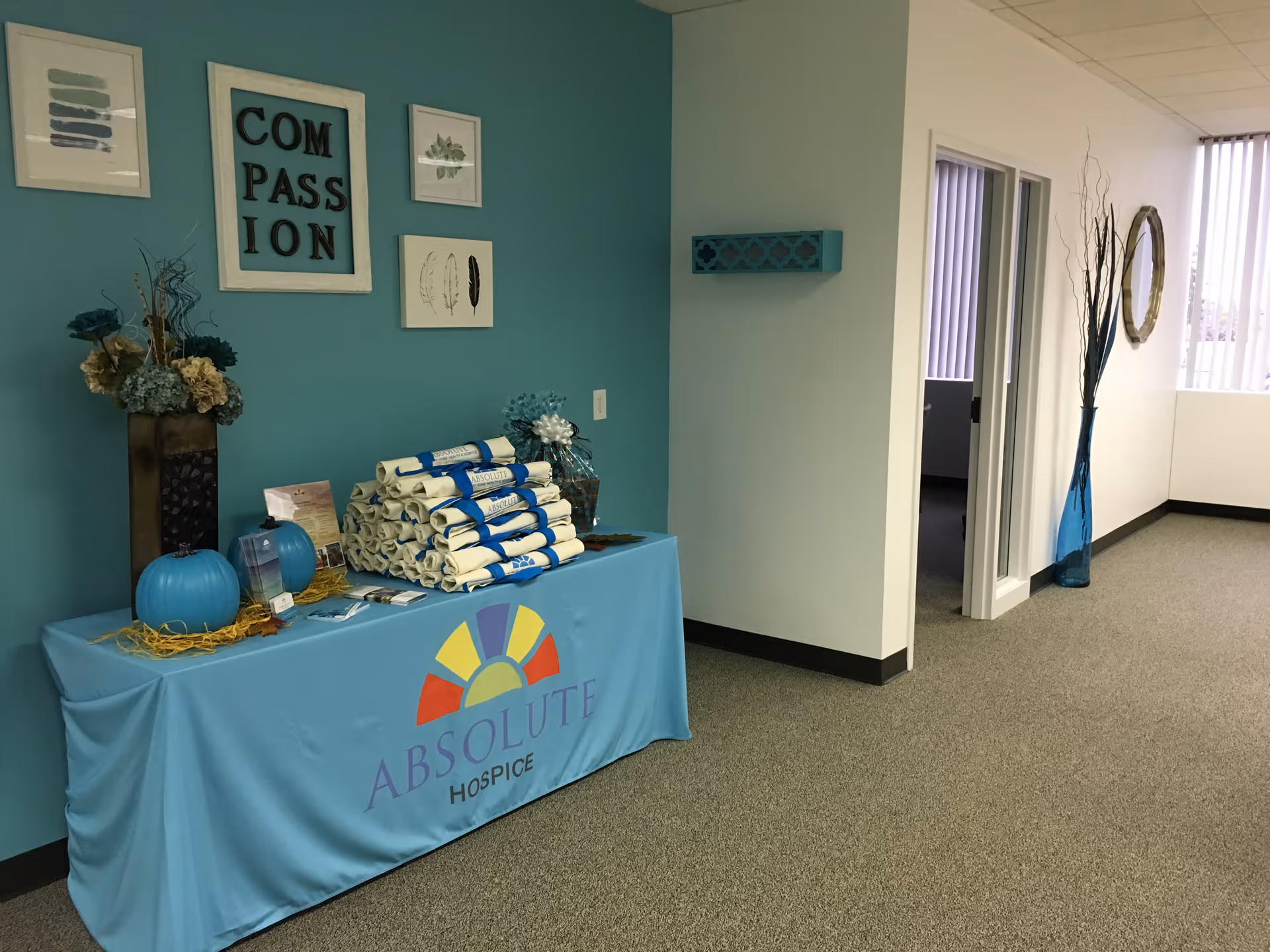 Teal display table in a hallway promoting Absolute Hospice with wall art.