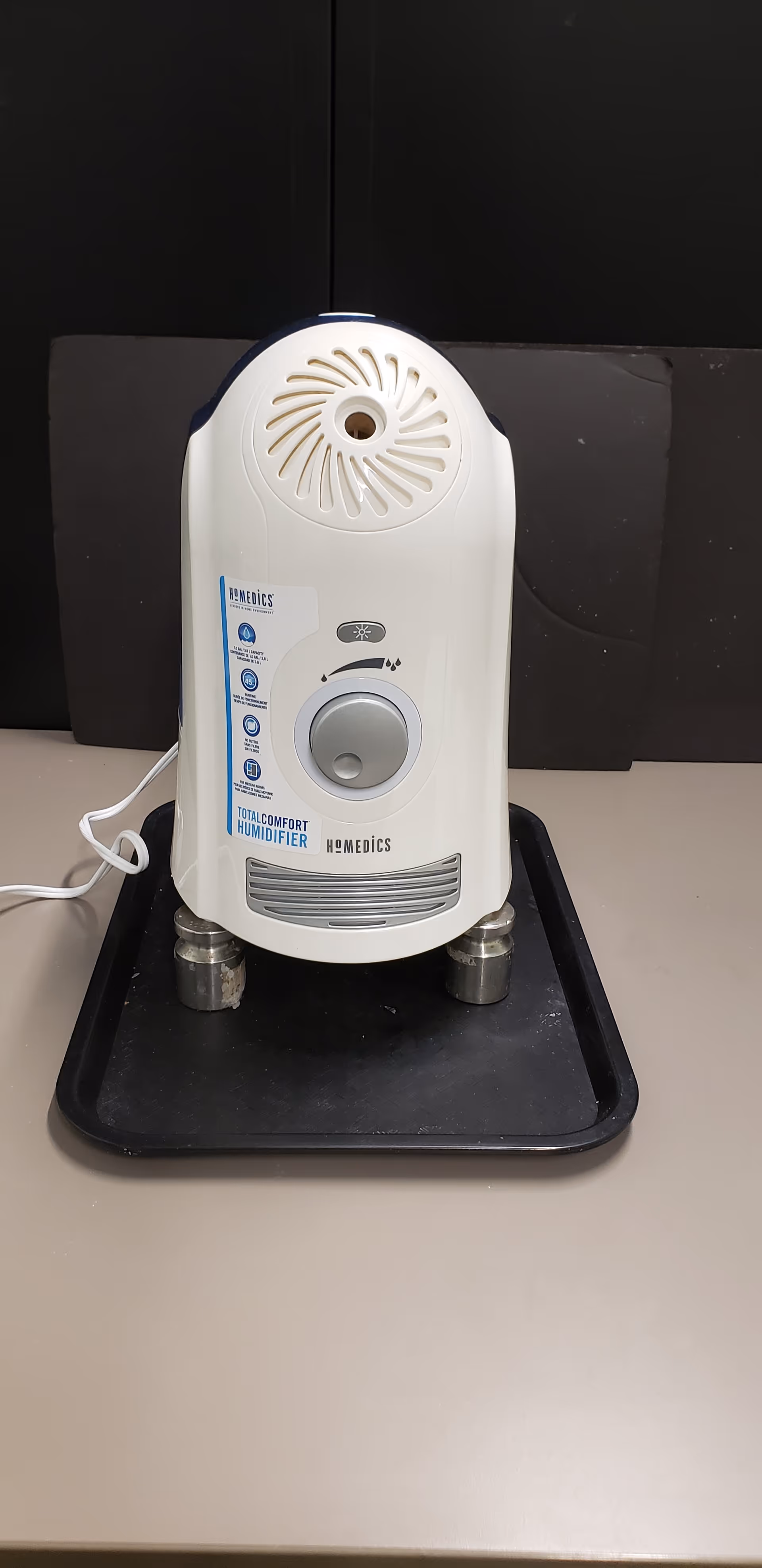White HoMedics humidifier sits on a black tray atop a beige counter.